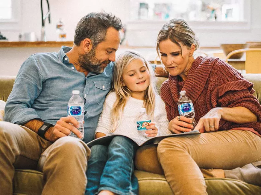family on couch reading book together while drinking nestle pure life purified water