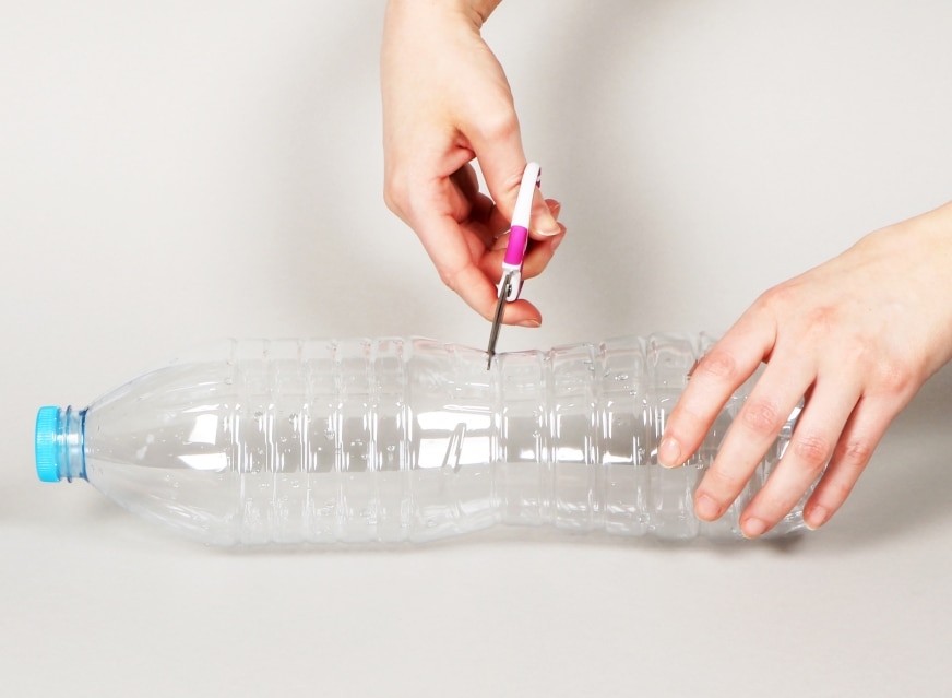 Découpe d'une bouteille d’eau en plastique avec des ciseaux pour fabriquer une horloge hydraulique.
