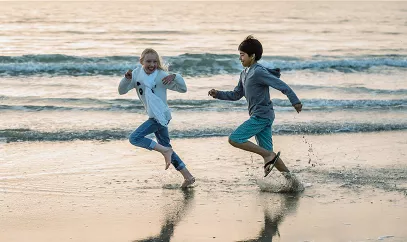 Two kids running actively and energetically on a beach alongside water