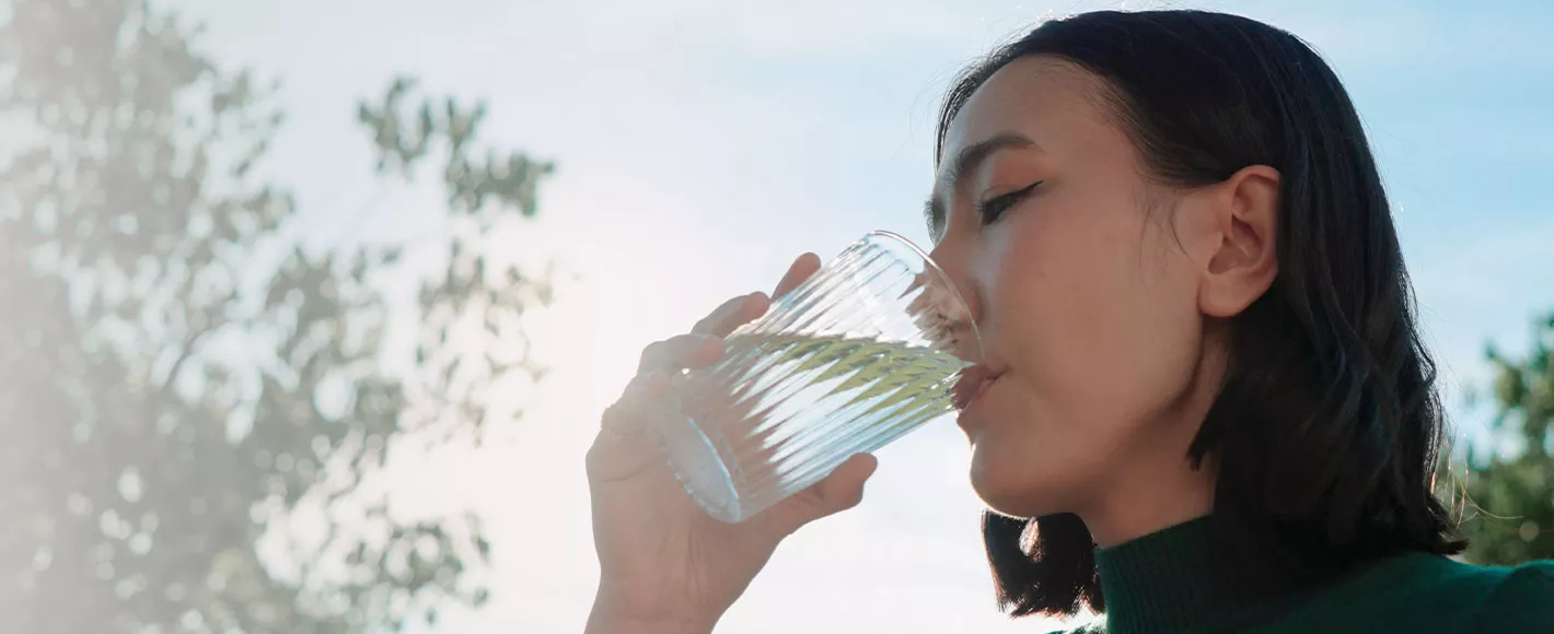Person drinking a glass of water outdoors to support everyday hydration