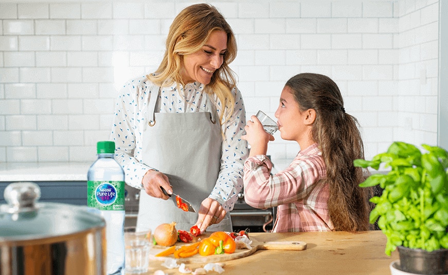 girl drinking Nestlé Pure Life Sparkling water in the kitchen with her mother
