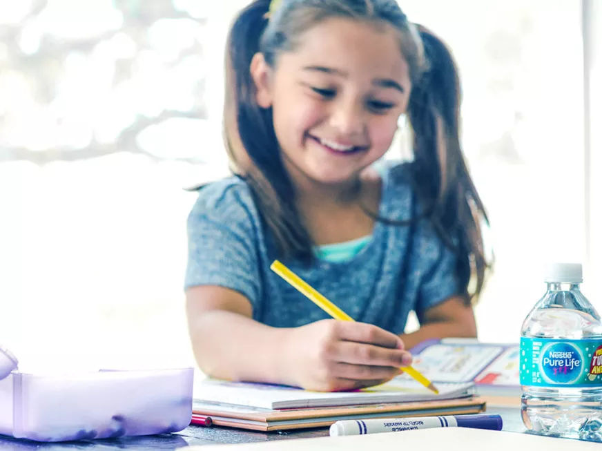 girl doing homework and with a mini bottle of nestle pure life purified water