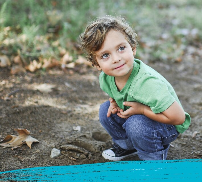 A child wearing a green t-shirt playing in the Australian bush